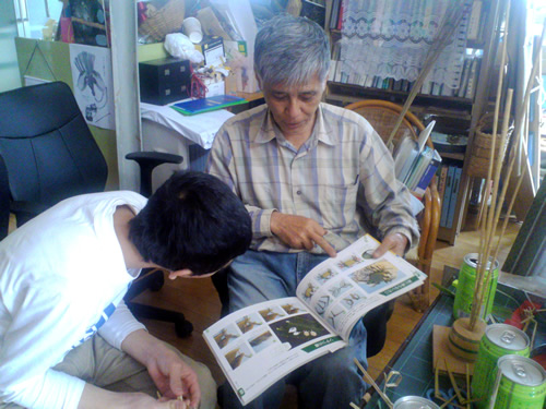 著書『手遊び草編み玩具』を開いて、草玩具の魅力を語る館長の新崎宏さん。