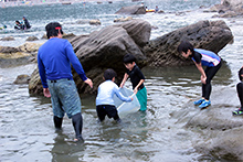 磯辺の潮溜まりで小魚やカニを捕る子どもたち。代表理事を務める関山隆一さんが子どもたちの遊びを見守る。